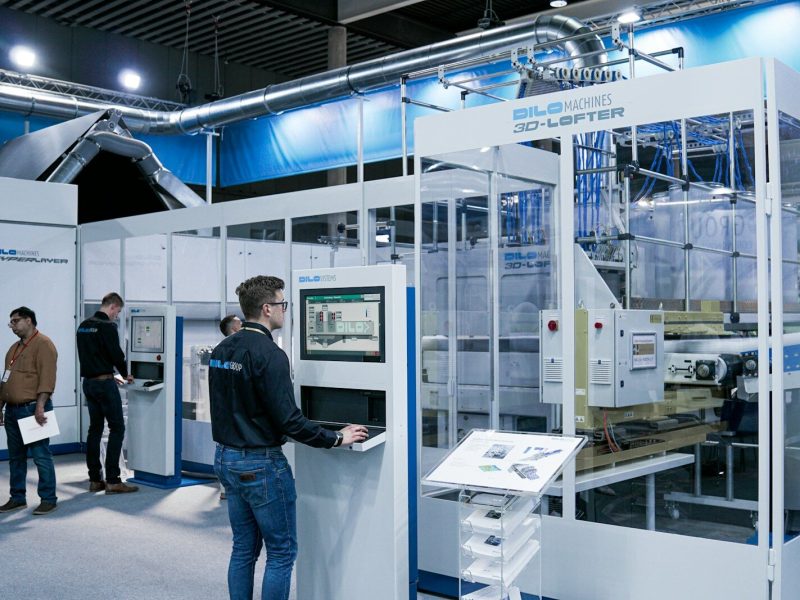 man standing while using computer and another group of men chatting